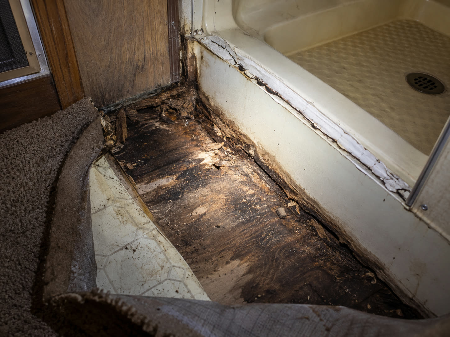 Rotted plywood subfloor beside an RV shower pan